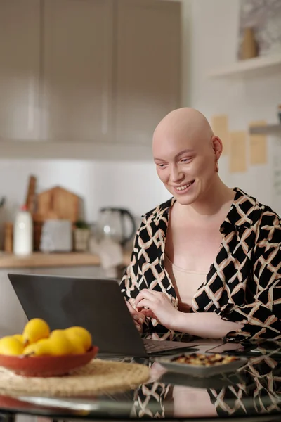 化学療法の後にはげ頭を持つ幸せな若い女性は オンライン映画を見ているか ビデオチャットで通信しながら ラップトップ画面を見て — ストック写真