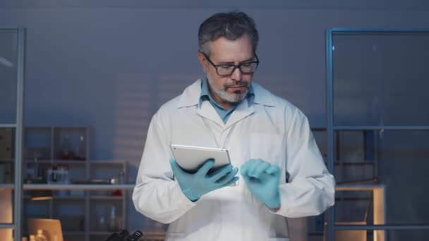 站在工作场所时 用数码平板电脑在实验室外套和手套中放置成熟的临床医生 并将培养皿与实验室生肉一起放回原处 — 图库视频影像