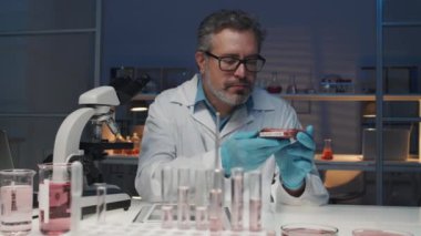 Kendine güvenen olgun bilim adamı laboratuvar ortamında yetişmiş etle petri kabını alır, özelliklerini öğrenir ve tablete yerleştirir, sonra mikroskoba bakar.