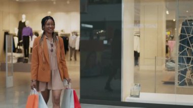 Mutlu Afrikalı Amerikalı genç bir kadın alışveriş merkezinde alışverişlerle yürüyor.