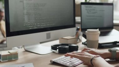 İşyerinde bilgisayar monitörünün önünde oturan, klavyeye yazı yazan orta ölçekli bir kadın, program için kod yazıyor.