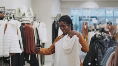 Afrikalı Amerikalı bir kadın internetten arkadaşına yeni kıyafetlerle ilgili danışmanlık yapıyor. Elinde akıllı telefon ve ona yeni gömlek gösteriyor.