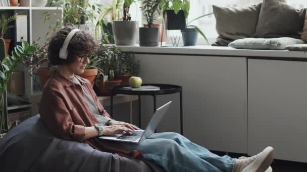 坐在扶手椅上 在现代办公室的笔记本电脑上与绿色植物一起工作的年轻女性 — 图库视频影像