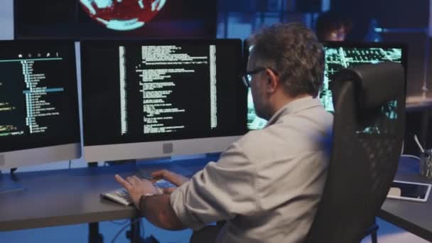 コンピュータプログラムのセキュリティのためのコンピュータにテーブルとタイピングコードに座っている成熟したプログラマのトリミングショット — ストック動画