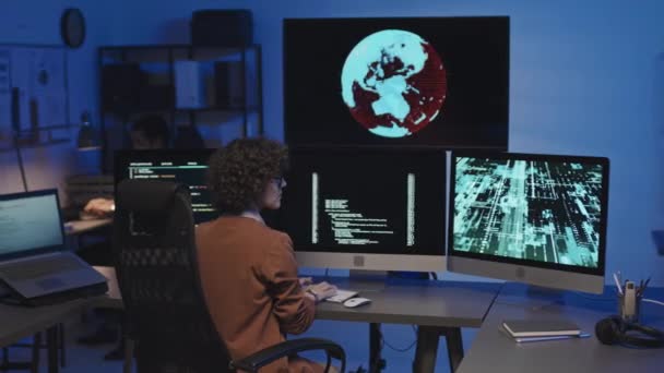 ビッグコンピュータモニターの前で椅子に座り 暗いItオフィスでの作業中にセキュリティコードを入力する若い女性のリアビュー — ストック動画