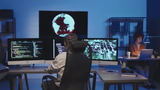 暗いItオフィスのモニター上のセキュリティコードでコンピュータで作業するプログラマーのグループの中型ショット — ストック動画