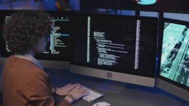 Geç saatlere kadar çalışması sırasında yeni yazılımlar geliştirmek için bilgisayarına güvenlik kodları yazan genç bir kadın programcının arka görüntüsü