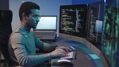 Geliştiricinin bilgisayar monitörleriyle masada oturup klavyeye yazarken orta boy görüntüsü, program için bilgisayar kodları yazar.