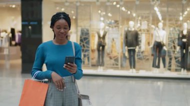 Alışveriş merkezinde akıllı telefon kullanırken kameraya gülümseyen Afrikalı Amerikalı kadın portresi