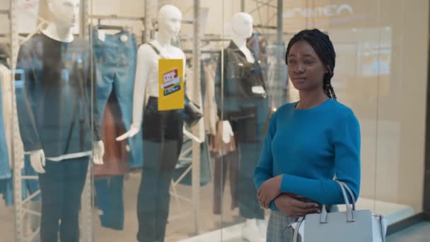 ショーケースに対してショッピングセンターに立っている間にカメラを見ている若いアフリカ系アメリカ人の女性の肖像画 — ストック動画