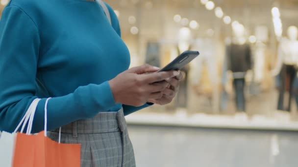 年轻女子站在商场时 与购物袋亲密接触 在智能手机上发短信 — 图库视频影像