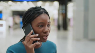 Genç Afrikalı Amerikalı kadın alışveriş merkezinde cep telefonuyla konuşuyor.