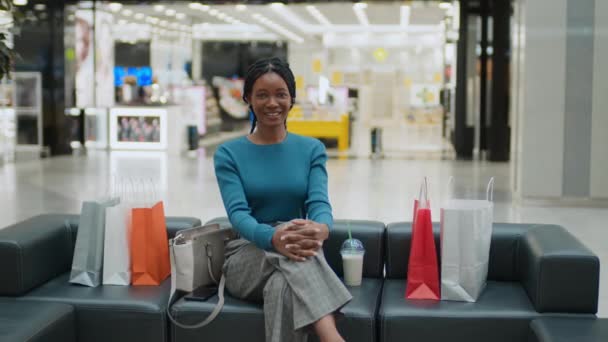 非洲裔美国妇女拿着购物袋坐在沙发上 购物后休息时对着相机微笑的画像 — 图库视频影像