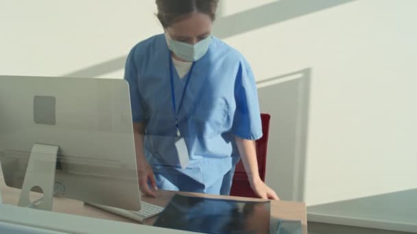 Felismerhetetlen Női Radiológus Kék Egyenruhát Védőmaszkot Visel Leül Asztalhoz Röntgenképekkel — Stock videók