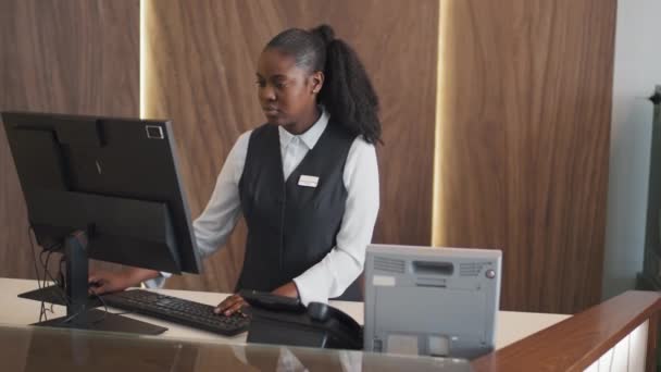 モダンなホテルでレセプションとして働くユニフォームを着ている若いアフリカ系アメリカ人女性 — ストック動画