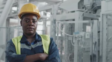 Üniforma giyen, fabrikada çalışan, kollarını kavuşturup kameraya bakan kendinden emin Afrikalı Amerikalı kadın mühendisin portresi.