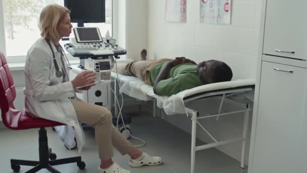 Зрелый Европеолог Консультирует Афроамериканца Лежащего Столе После Ультразвукового Сканирования Щитовидной — стоковое видео