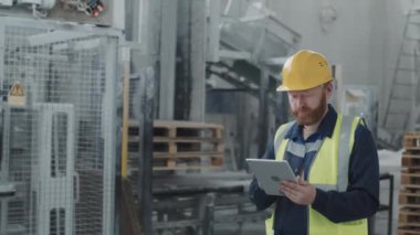 Fabrika atölyesindeki endüstriyel makineleri kontrol etmek için dijital tablet kullanan beyaz adamın görüntüsü.
