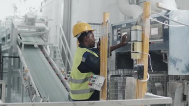 Siyah kadın mermer fabrikasında çalışıyor. Meslektaşıyla telsizle konuşuyor ve makinenin ayarlarını değiştiriyor.