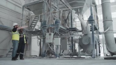 Düşük açılı etnik çeşitlilikteki fabrika işçilerinin üretim sürecini tartışmak üzere makinelerle donatılmış atölye boyunca yürümeleri