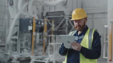 Modern fabrikada dijital tablet kullanarak çalışan olgun sakallı beyaz teknisyenin seçici odak portresi