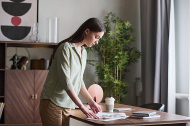 Genç bir iş kadınının ofiste çalışırken masanın üzerine eğilmesinin ve çizimlere bakmasının yan görüntüsü.