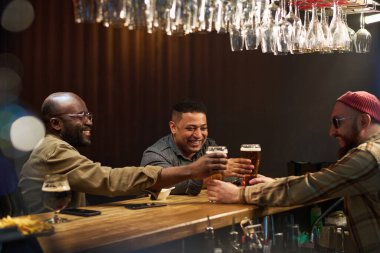 Güneş gözlüklü, bereli ve gömlekli sakallı barmen, bar tezgahının yanında duran kültürler arası neşeli arkadaşlara iki bardak bira uzatıyor.
