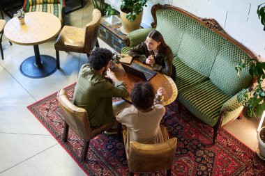 Kültürler arası birkaç genç arkadaşın masanın üstünde oturmuş sohbet ederken biri dizüstü bilgisayarın başında oturup adama bakıyor.