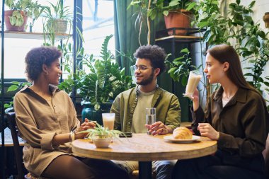 Kültürler arası hayvanat bahçesinde kahve içip sohbet ederken gözlüklü genç bir adam mutlu kız arkadaşına bakıyor.