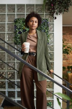 Zarif giyimli genç Afrikalı Amerikalı iş kadını merdivenlerin arasında duruyor ve kameraya bakıyor.