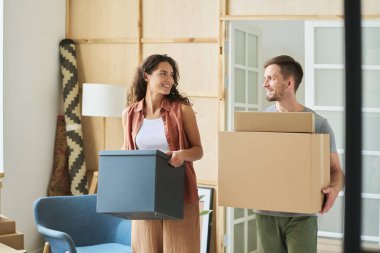 Yeni dairelerine taşınırken karton kutular taşırken mutlu genç karı koca birbirlerine bakıyor.