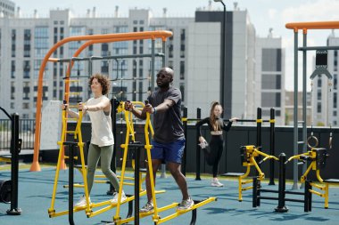 Genç Afrikalı Amerikalı erkek ve aktif giyimli bir grup kadın şehir merkezindeki spor tesislerinde kol ve bacak eğitimi alıyorlar.