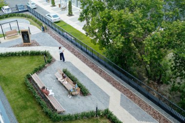 Yeşil çimenleri, ağaçları ve çalıları olan, gri taşlar ve tuğla yollar boyunca büyüyen, insanların yürüdüğü ve oturduğu büyük bir parkın bir parçası.