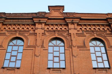 Kırmızı tuğladan yapılmış tarihi anıtın altında modern şehrin eski bölümünde mavi gökyüzüne bakan üç pencere var.