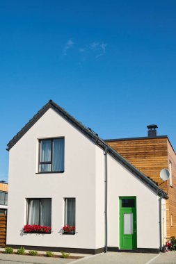 Kırsal alanda canlı mavi gökyüzüne karşı duran üç pencereli ve kapalı yeşil kapılı beyaz tek kulübenin ön manzarası