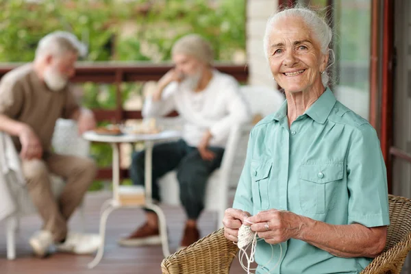 一位快乐的老年女性 白发苍苍 坐在养老院阳台上的柳条扶手椅上 头戴针织围巾 看着相机 — 图库照片