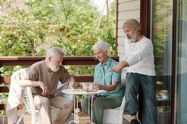 上了年纪的男人 留着灰胡子 一边指指棋盘 一边问老妇人在退休的家里下棋时应该做些什么 — 图库照片