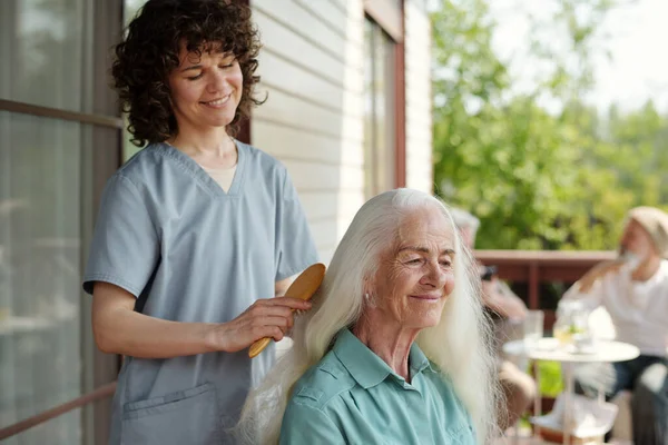 Jovem Cuidador Morena Feliz Escovando Longos Cabelos Brancos Paciente Sênior — Fotografia de Stock