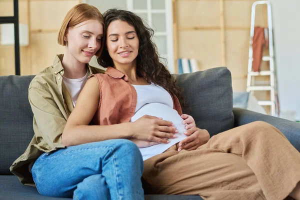 新居新居后 快乐的年轻黑发孕妇和她深情的女友坐在沙发上享受着休息 — 图库照片