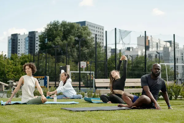 一群身穿运动服 活跃在不同文化间的年轻人坐在运动场绿色草坪上的垫子上进行体育锻炼 — 图库照片