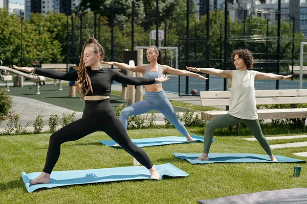 三个年轻的女运动员在室外草地上训练时 穿着运动服 在垫子上进行体育锻炼时张开双臂 — 图库照片