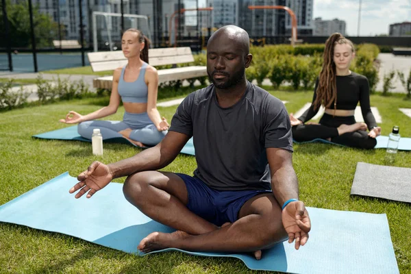 年轻的非洲裔美国男子瑜伽教练与两名年轻的女运动员对坐 穿着紧跟在他后面的动作重复练习 — 图库照片