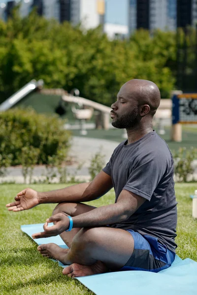 在露天瑜伽练习中 年轻的非洲裔美国人穿着活动服坐在垫子上打坐时的侧视图 — 图库照片