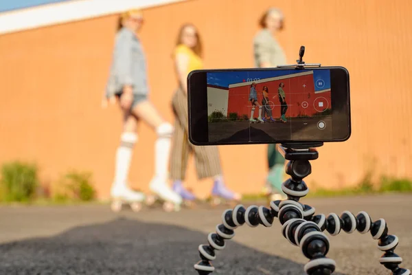 Fokus Stativ Med Smartphone Videofilmning Tre Unga Vänliga Kvinnliga Rullskridskoåkare — Stockfoto