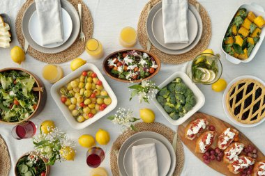 Tabağında peçeteler, taze limonlar, ev yapımı sebzeler, salatalar, sandviçler, meyve suyu, limonata ve tatlı turtalar olan servis edilen yemek masasının en üst görüntüsü.