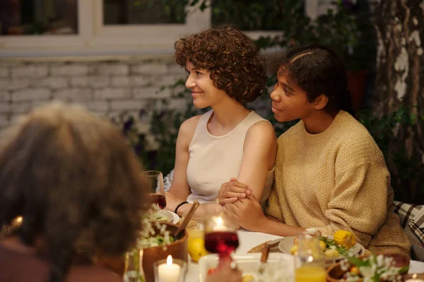 在户外家庭晚宴上 年轻的黑发女子和她可爱的女儿坐在餐桌旁 与人聊天的侧影 — 图库照片