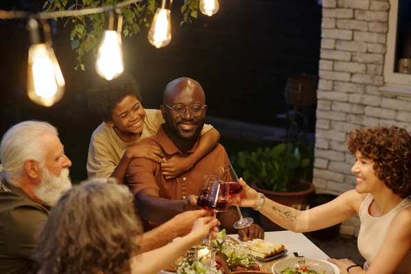 Happy young man with son toasting with his wife over served table during outdoor family dinner while enjoying spending time together
