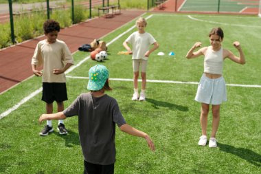 Aktif kıyafetli okul çocuğunun sınıf arkadaşlarının önünde dikiz aynasıyla onlara yeni fiziksel egzersizler gösterirken ondan sonra tekrar ediyorlar.
