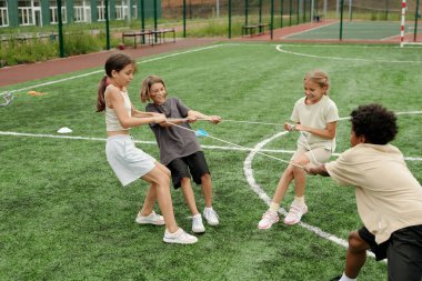 Yeşil futbol sahasında durup maçtan önce antrenman yaparken spor kıyafetli dört sevimli okul çocuğu stadyumda ip çekiyorlar.