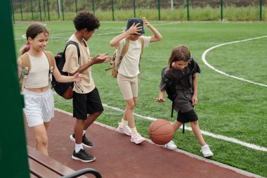 Dört aktif çocuk tişört ve şortlarıyla modern stadyumdaki yeşil futbol sahasında ilerleyip bir şeyler tartışıyorlar.